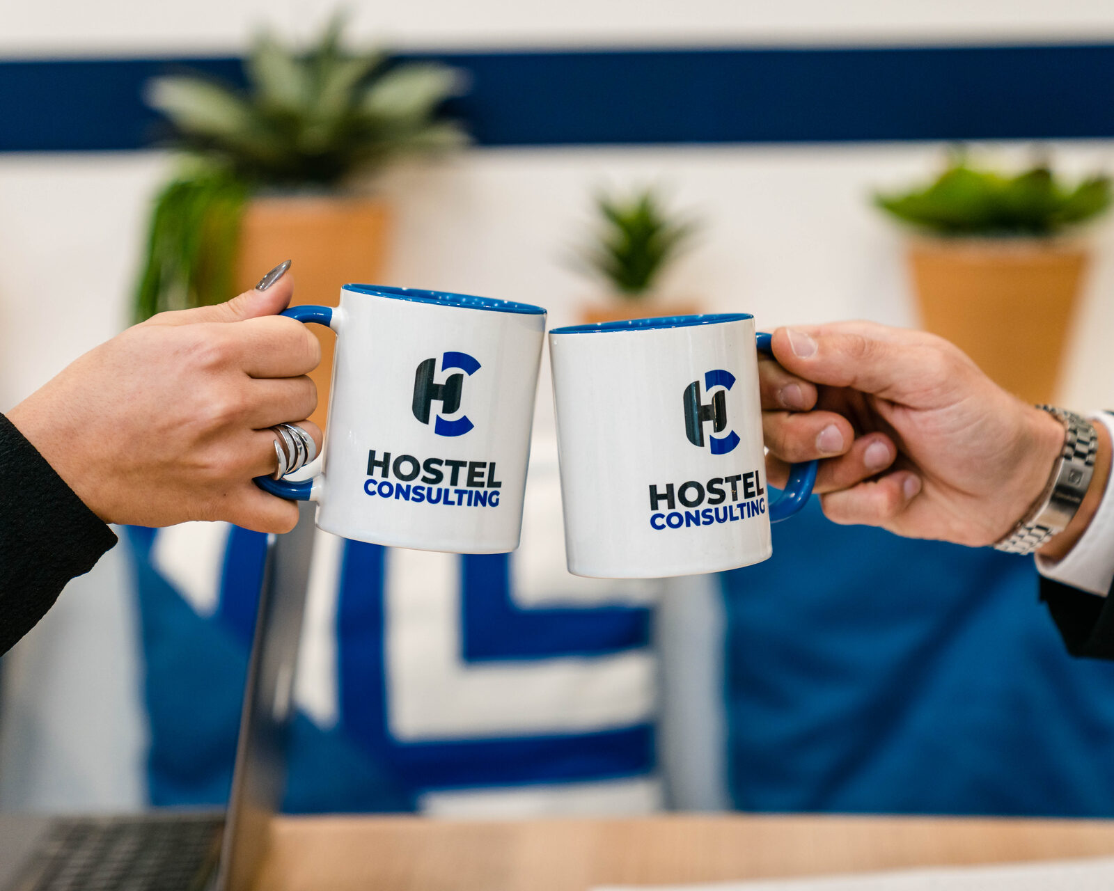 Deux mains trinquent avec des mugs Hostel Consulting
